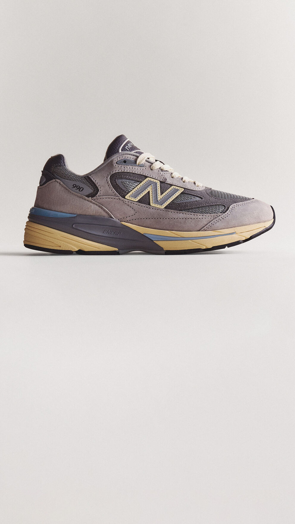 A grey 990v7 sneaker sitting on a grey studio backdrop.