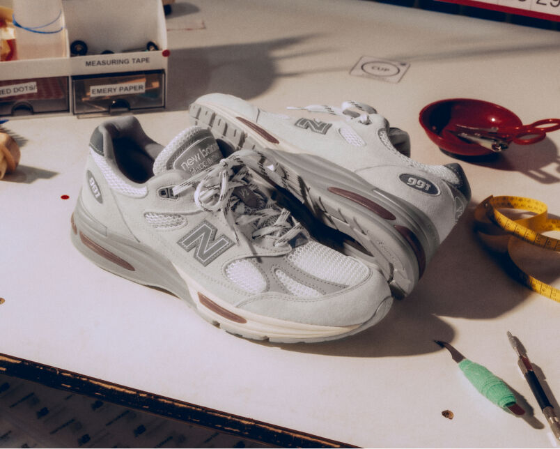 A pair of New Balance Made in UK sneakers in front of a rabbit in a brown textured studio environment. 