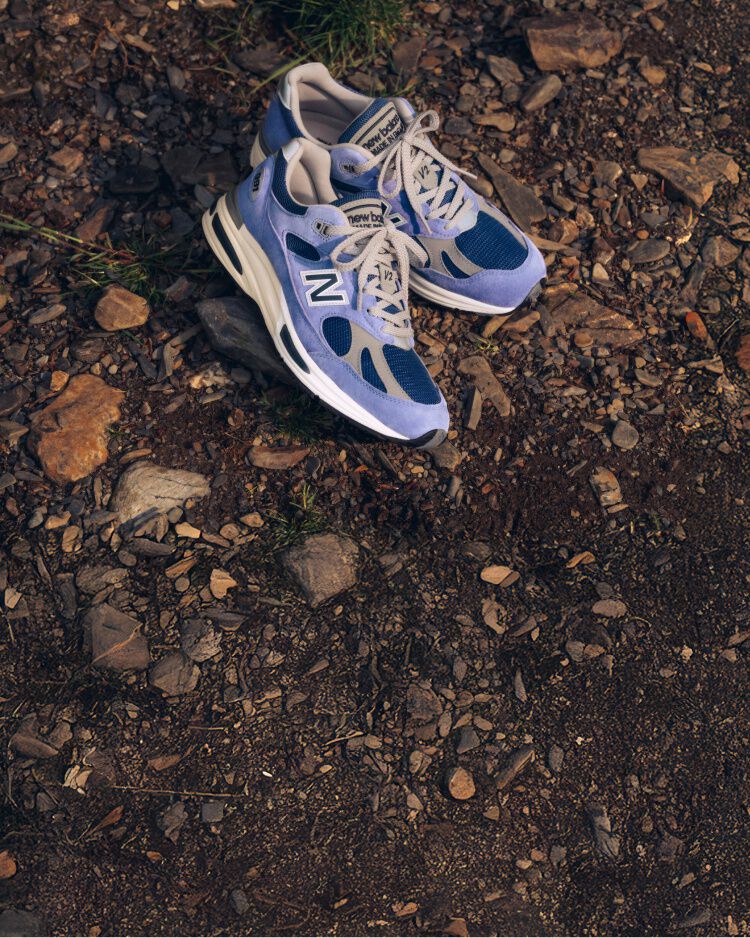 A pair of New Balance Made in UK sneakers on a raw earth surface of dirt and stones. 