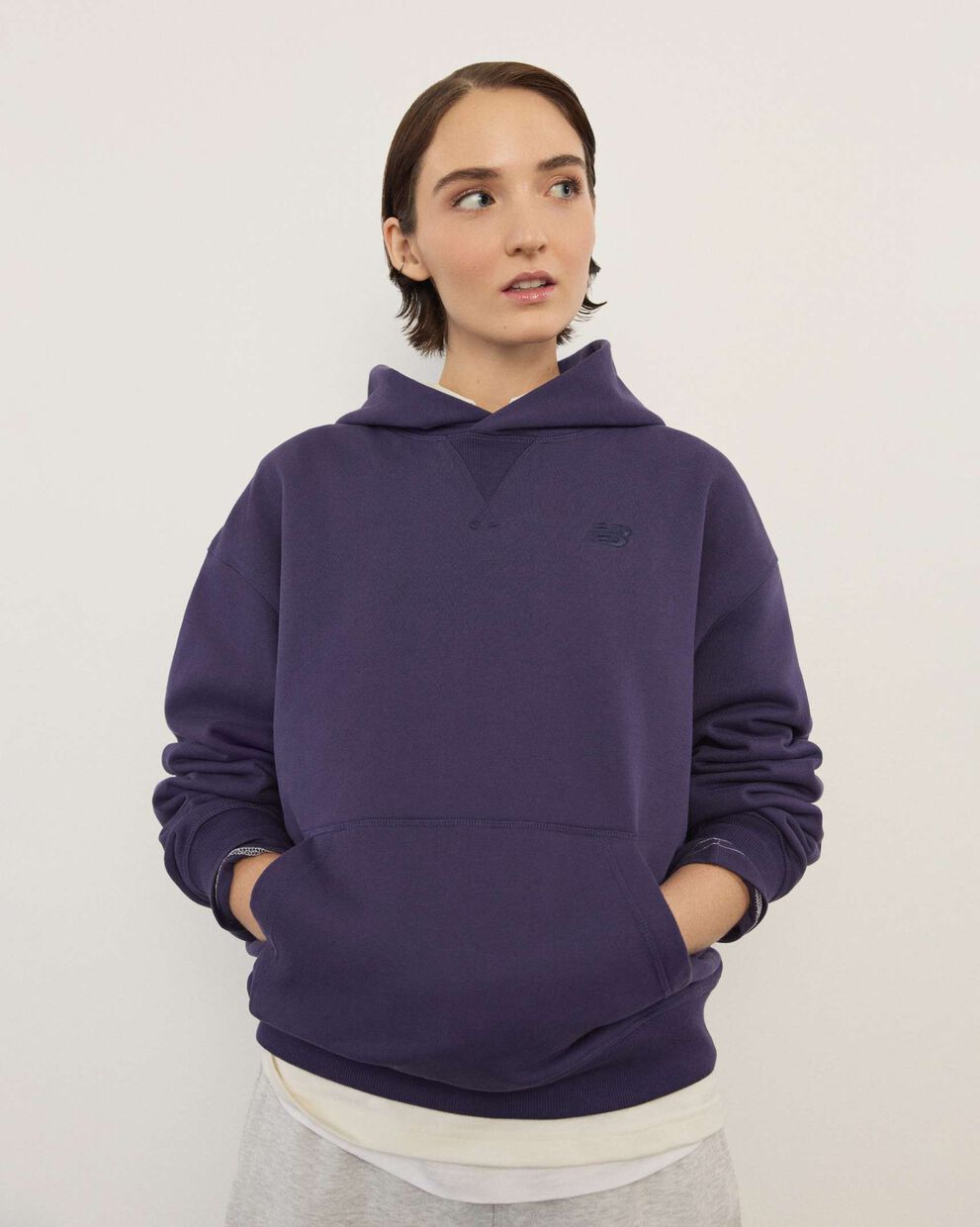 A woman wearing New Balance standing in front a white wall.