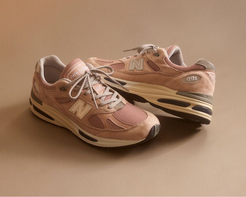 A pair of New Balance Made in UK sneakers in front of a rabbit in a brown textured studio environment. 