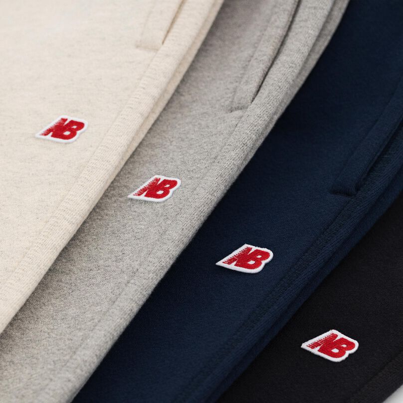 Close up image of stacked MADE in USA sweatpants, showing the New Balance logo on each.