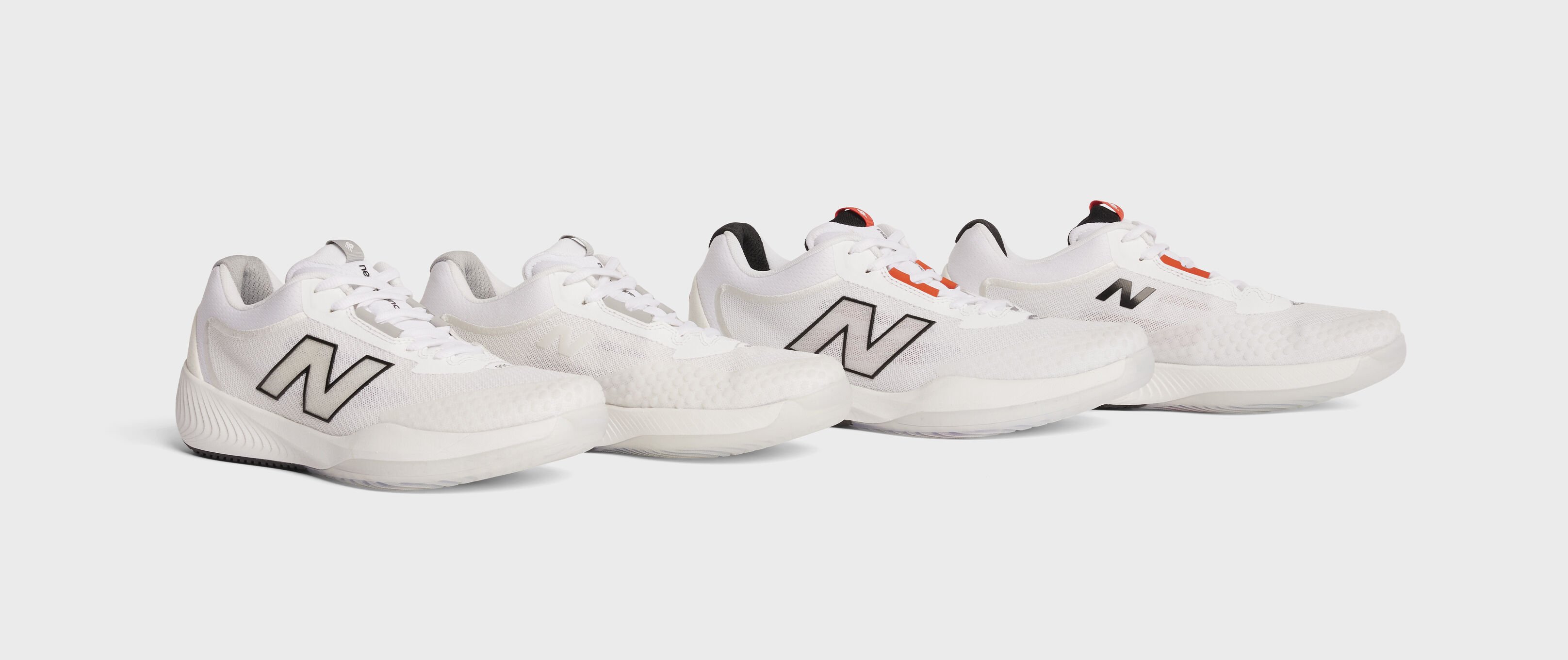 Men's and women's all white tennis shoes sitting on a grey background.