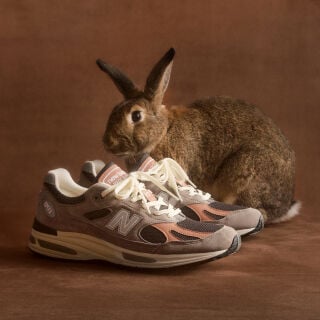 A pair of New Balance Made in UK sneakers in front of a rabbit in a brown textured studio environment. 