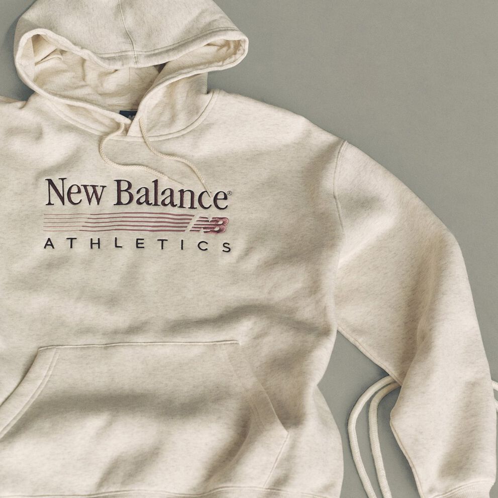 Flat lay studio image of a light beige hooded sweatshirt placed on a smooth, light gray background.