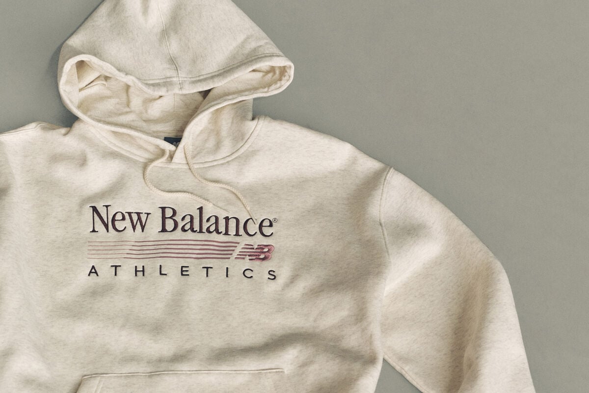 Flat lay studio image of a light beige hooded sweatshirt placed on a smooth, light gray background.