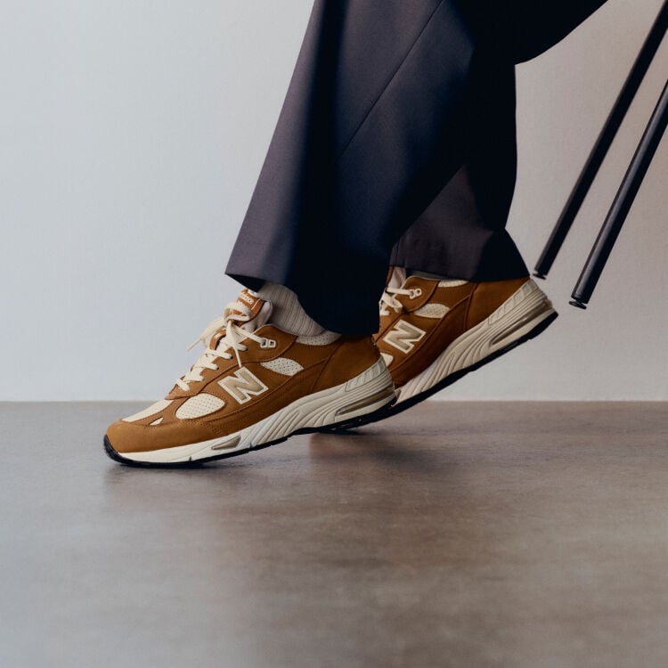 Knee down view of a man wearing a pair of New Balance Made in UK sneakers in with room with a concrete floor and white walls. 