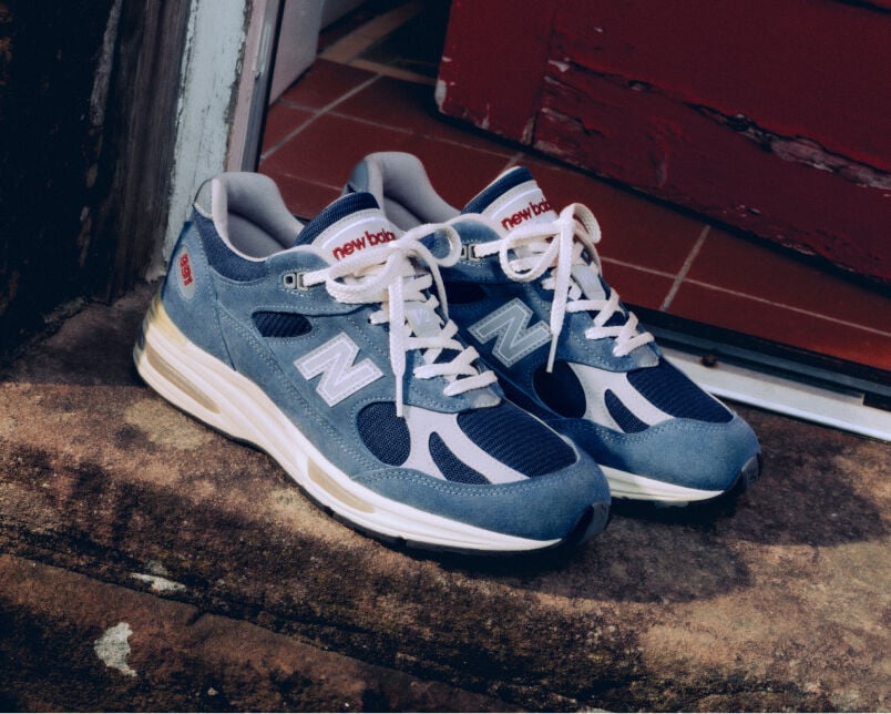 A pair of New Balance Made in UK sneakers in front of a rabbit in a brown textured studio environment. 