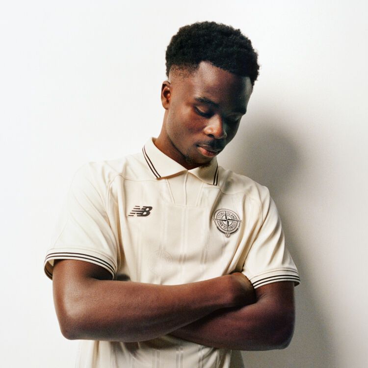 Saka looking down with his arms folded wearing a beige jersey. 